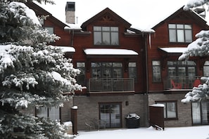 Cozy cabin with a balcony and chimney, surrounded by snow-covered trees.