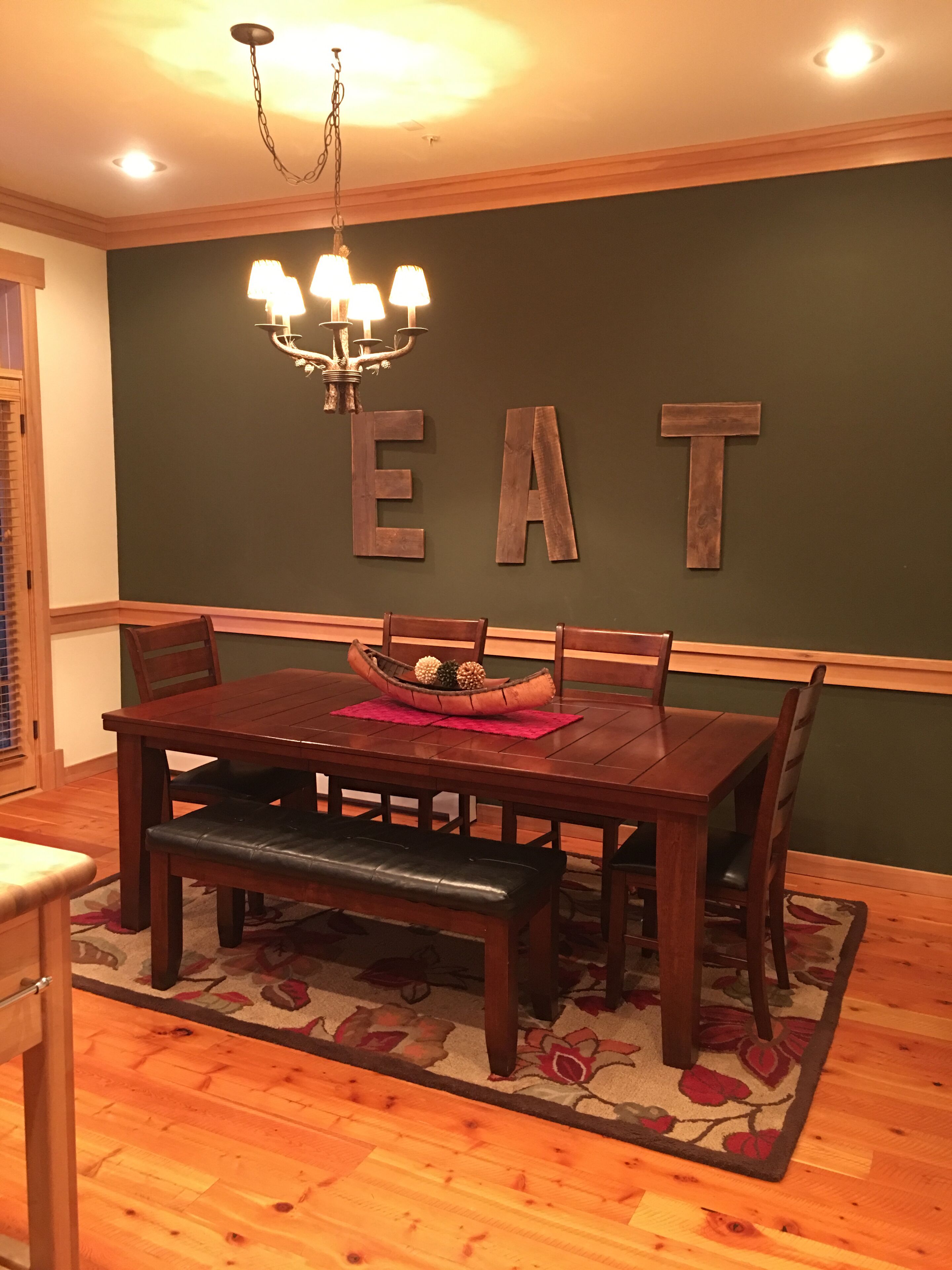 A dining area with a wooden table, chairs, a chandelier, and a wall with the word "EAT" spelled out in large letters.