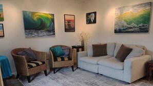 A living room with a white sofa, two wicker chairs, a coffee table, and artwork on the walls.