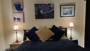 A bedroom with a bed, two bedside lamps, a nightstand, and wall art.