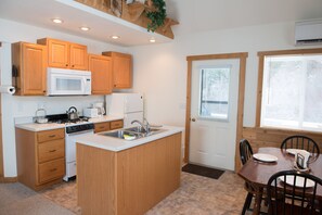 A kitchen with wooden cabinets, a microwave, stove, sink, and a dining area with a table and chairs.
