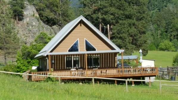 A wooden cabin with a triangular roof, a covered porch, and a fenced deck.