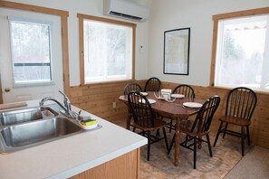 A kitchen with a sink, wooden chairs, a dining table, and windows with blinds.