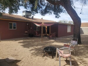 A covered patio area with outdoor furniture, a fire pit, and a building with a red exterior.