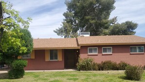 A two-story house with a red brick exterior, a brown roof, and a small front yard with grass and shrubs. - Pet-friendly, Family-friendly & Fun-Friendly Central-to-Everything Phoenix Home (Phoenix)