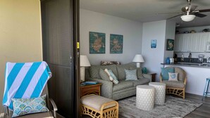 Ein Wohnzimmer mit einer Couch, zwei Beistelltischen, einem Sessel, einem kleinen runden Tisch und einer Küchenzeile mit Schränken und einer Arbeitsfläche.