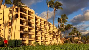 Ein mehrstöckiges Hotel mit Balkonen, umgeben von Palmen und Grünpflanzen.