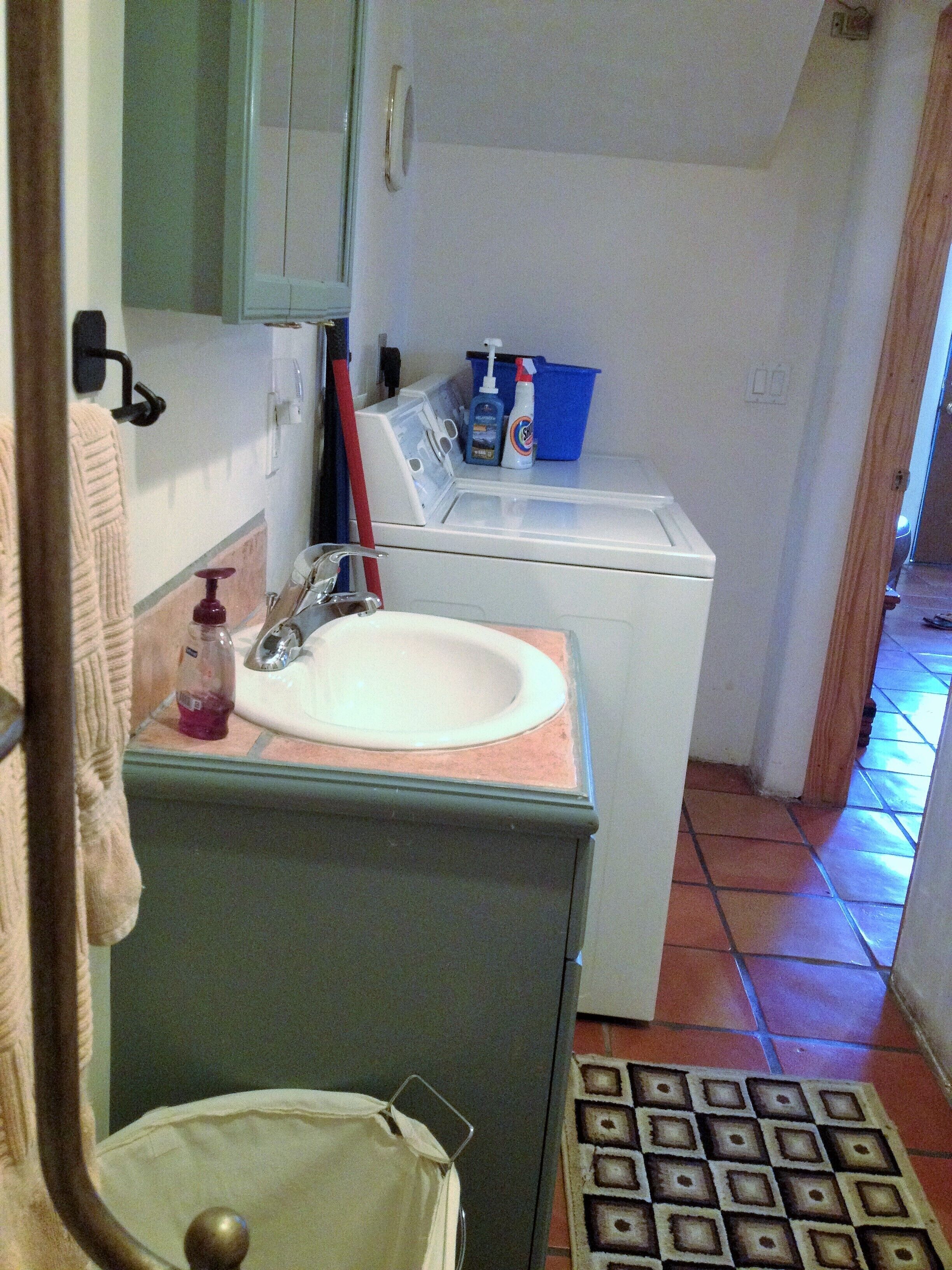 A compact bathroom with a sink, mirror, and a washing machine.