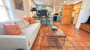 A living room with a sofa, a coffee table, and a kitchen in the background. - Casita F - 2 Bed, 1.5 Bath (Two Story) (Santa Fe)