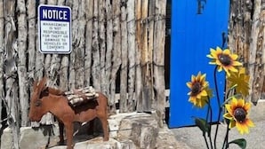 A rustic wooden fence with a blue gate, a wooden horse sculpture, and a potted sunflower arrangement. - Casita F - 2 Bed, 1.5 Bath (Two Story) (Santa Fe)
