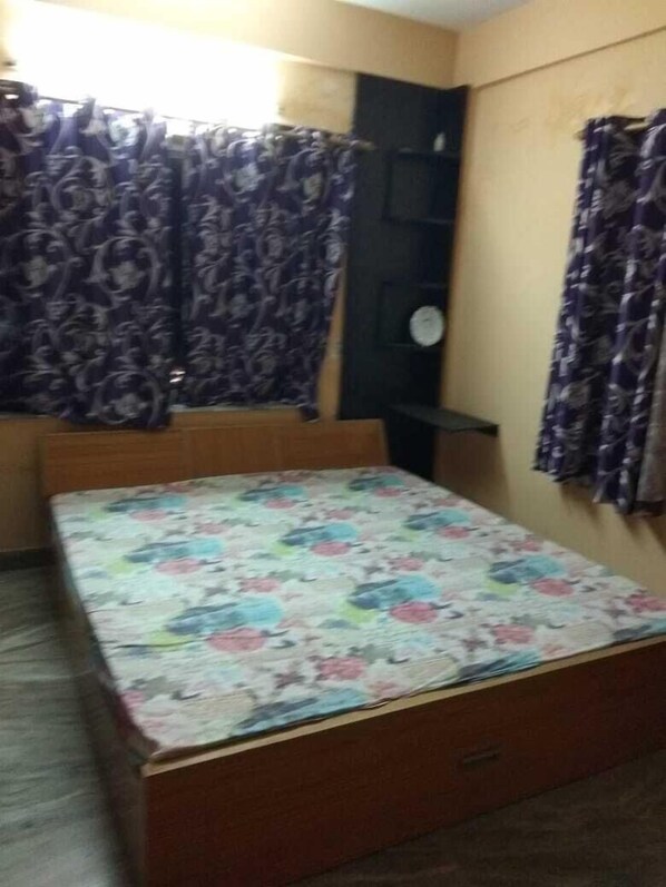 A bedroom with a bed, a wardrobe, a small window with curtains, and a wall-mounted clock.