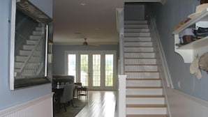 Un escalier menant à un deuxième étage, un coin repas avec une table et des chaises, et une fenêtre donnant sur un paysage verdoyant.