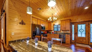 L’intérieur d’une cabane en bois, avec un îlot en granit, des armoires en bois et un lustre.