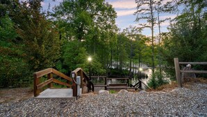 Une terrasse en bois avec un banc, entourée d’arbres et bordée d’un chemin de gravier.