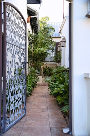Un sendero pavimentado estrecho que conduce a una entrada con portón y un decorativo cerramiento de metal.
