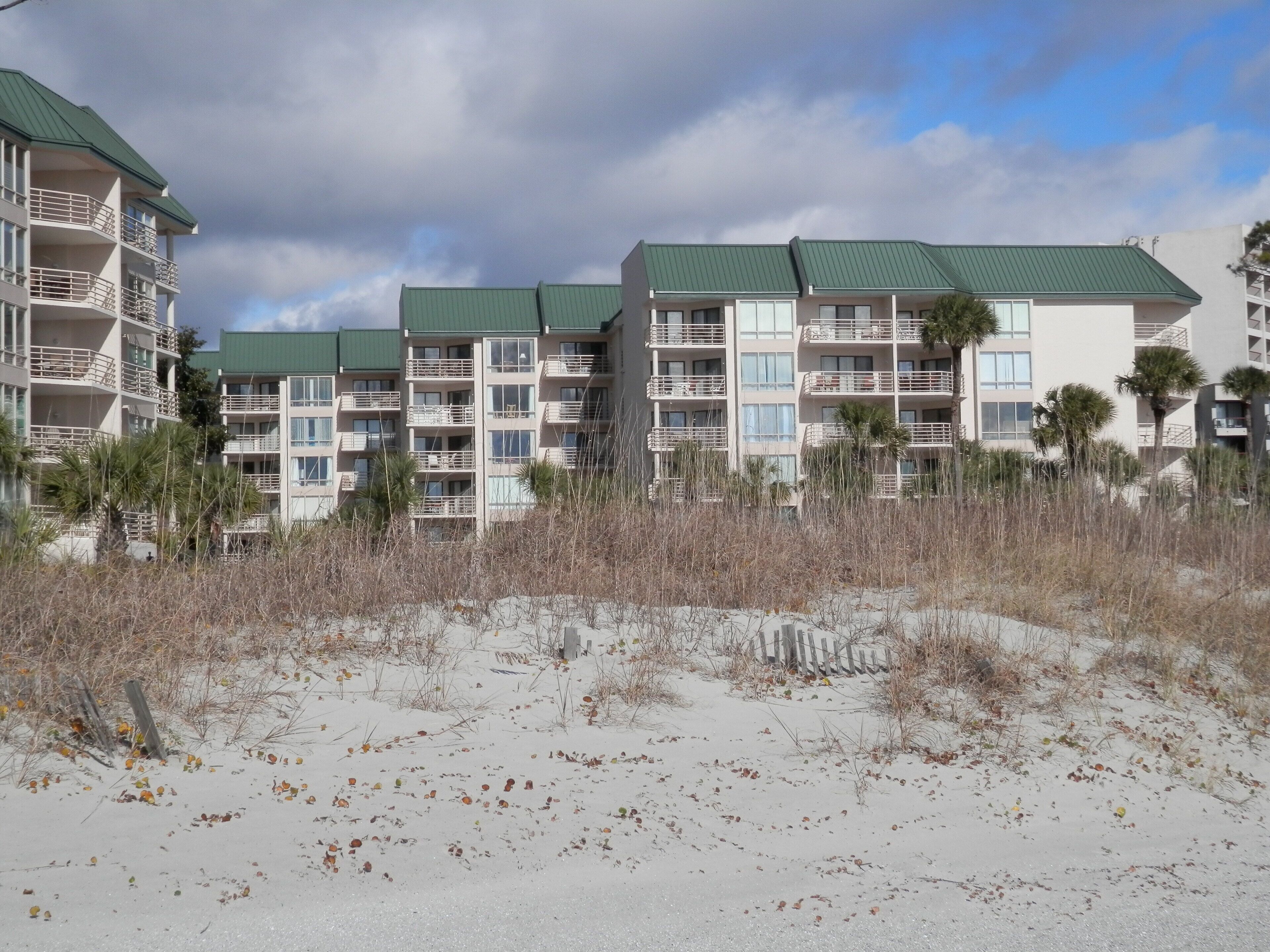 Un hôtel situé en bord de mer, doté de nombreux balcons, d’une plage de sable en contrebas et offrant une vue sur un ciel dégagé.