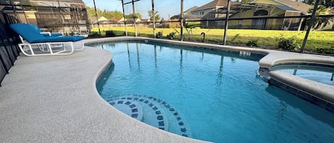 Una piscina de borde curvo, una silla de descanso y una zona cubierta con vistas a casas al fondo.