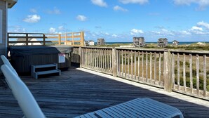 Eine Holzterrasse mit Bank und Whirlpool mit Blick auf einen Strand, an dem Häuser und Dünen liegen.