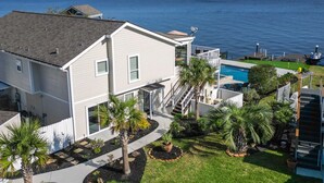 Una casa de dos plantas con piscina, rodeada por un jardín cuidado con palmeras y vistas al mar.