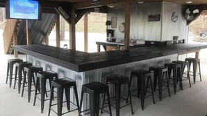 A bar area with a long counter, multiple stools, a television displaying a hotline, and signs indicating Bourbon Street location. - Cozy Cabin center of Bourbon Trail, Near Bardstown, beautiful country views (Springfield)