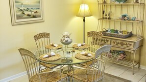 A dining area with a glass-top table surrounded by wicker chairs, a chandelier, a lamp, and a decorative shelf with fish-themed items.