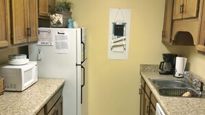 A compact kitchen with wooden cabinets, a refrigerator, a microwave, and a coffee maker.