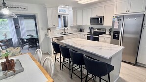 A modern kitchen with white cabinets, a large island with bar stools, a built-in microwave, and a stainless steel refrigerator.