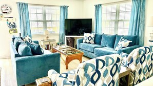 A living room with a sofa set, a coffee table, a television, and a wall clock.