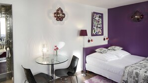 Une chambre moderne avec un lit, une table en verre avec des chaises, un mur d’accent violet et un élément décoratif mural.