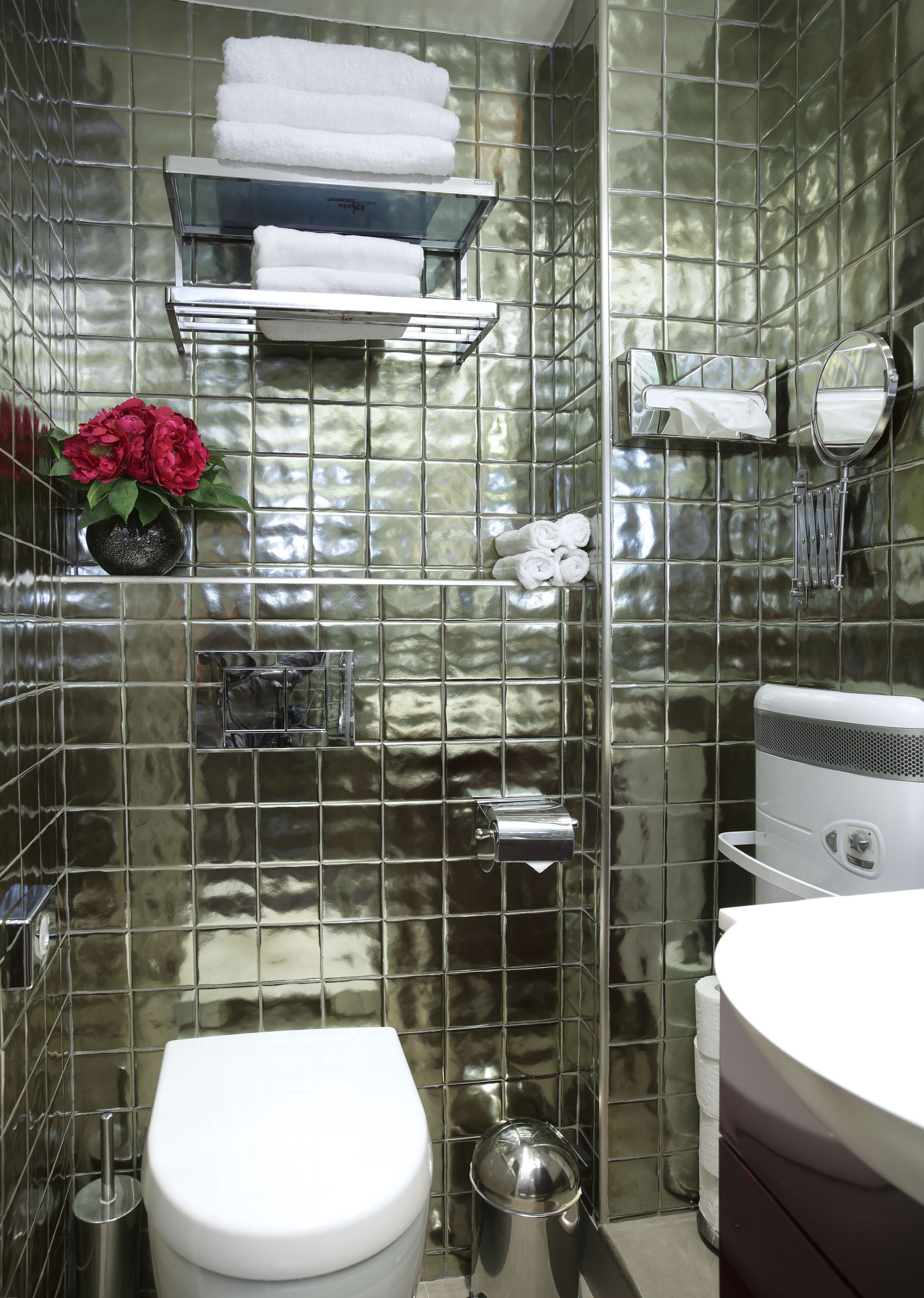 Modernilla designilla varustettu kylpyhuone, jossa on wc, pesuallas, peili sekä hylly, jossa on pyyhkeitä ja maljakko kukkia.