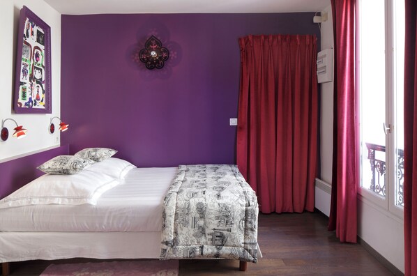 Un dormitorio con cama, paredes moradas, un adorno en la pared y una ventana con cortinas rojas.