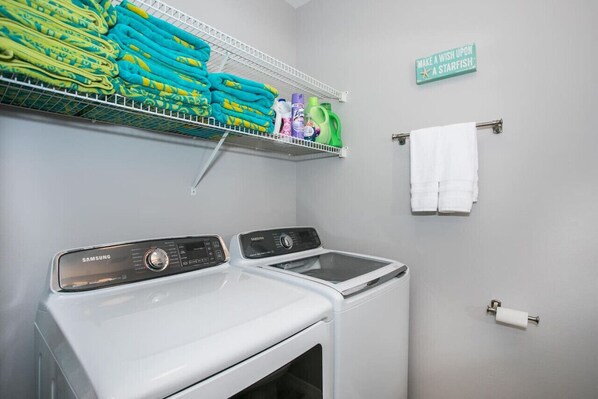 A laundry room with two Samsung washing machines, a shelf with folded towels, cleaning supplies, and a sign that says "Make a wish upon a starfish." - Sea Salt Cottage: Amazing home located on the Gulf of Mexico. Sleeps 13 comfortably! (Navarre)