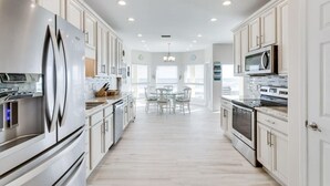 Une cuisine moderne avec des meubles blancs, des appareils en acier inoxydable et un îlot central doté de sièges.