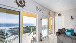 Un vaste espace de vie avec une grande porte-fenêtre coulissante donnant sur un balcon avec vue sur l’océan.