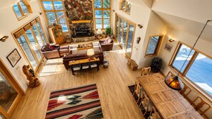 A spacious loft with a stone fireplace, wooden furniture, and large windows offering views of the outdoors. - Ski-in, Quick Walk to Slopes with AMAZING VIEWS (Mt Crested Butte)
