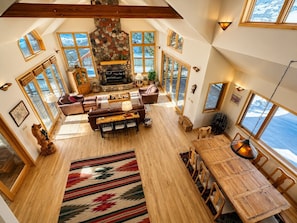 A spacious loft with a stone fireplace, wooden furniture, and large windows offering views of the outdoors. - Ski-in, Quick Walk to Slopes with AMAZING VIEWS (Mt Crested Butte)
