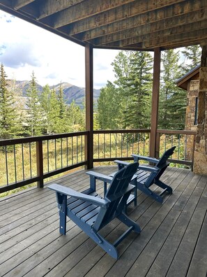 A wooden deck with two Adirondack chairs, a stone building, and a mountainous landscape in the background. - Ski-in, Quick Walk to Slopes with AMAZING VIEWS (Mt Crested Butte)