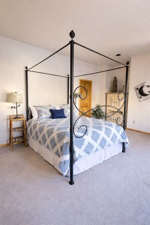 A four-poster bed with a geometric patterned bedspread, a bedside table with a lamp, and a wall-mounted cabinet.