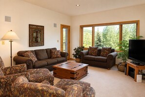 A living room with two sofas, a coffee table, a television, and a large window with a view of trees. - Ski-in, Quick Walk to Slopes with AMAZING VIEWS (Mt Crested Butte)