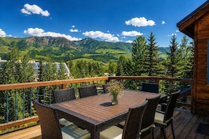 A wooden deck with a table and chairs, overlooking a mountainous landscape.