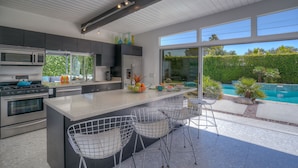 A modern kitchen with a large island, stainless steel appliances, and a view of a swimming pool. - PS Butterfly: Well-Styled, Authentic Mid-Century Home (Palm Springs)
