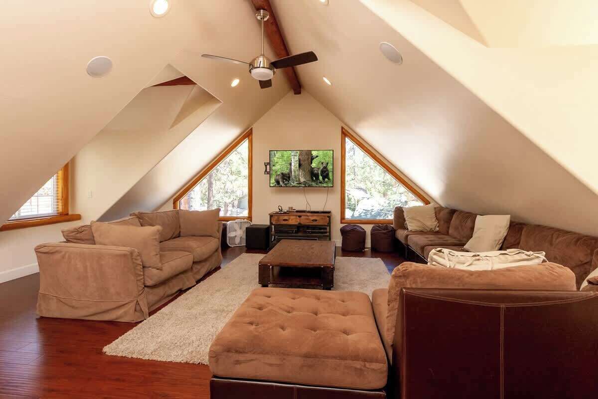 Un salón acogedor tipo loft, con techo alto, vigas de madera y ventanas amplias.
