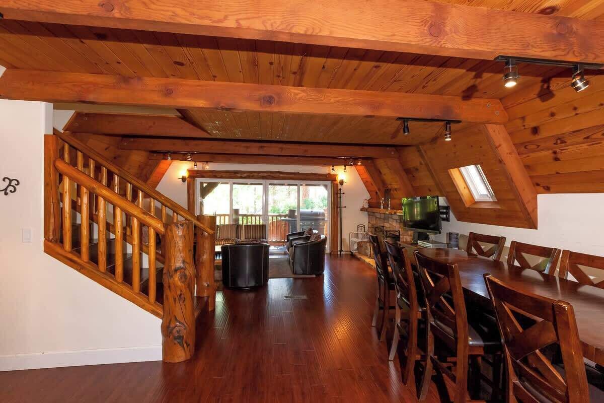 Interior de madera con una escalera, comedor y vistas al exterior.