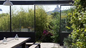 Eine Terrasse im Freien mit Holztisch und -bänken, umgeben von üppiger Vegetation und Blick auf ferne Hügel.