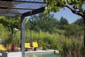 A pool area with yellow lounge chairs, a pergola, and lush greenery in the background. - Stunning and spacious home in Provence! (Lourmarin)