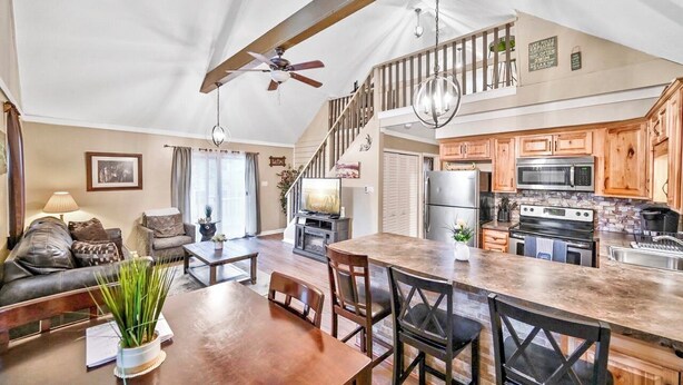 A spacious living area with a dining table, wooden chairs, a sofa, and a ceiling fan. A kitchen with wooden cabinets and modern appliances is visible in the background. - Beach/Lake Home In Towamensing Trails (Albrightsville)
