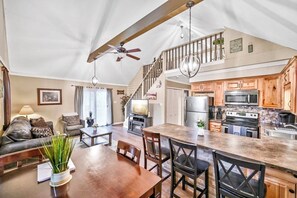 A spacious living area with a dining table, wooden chairs, a sofa, and a ceiling fan. A kitchen with wooden cabinets and modern appliances is visible in the background. - Beach/Lake Home In Towamensing Trails (Albrightsville)