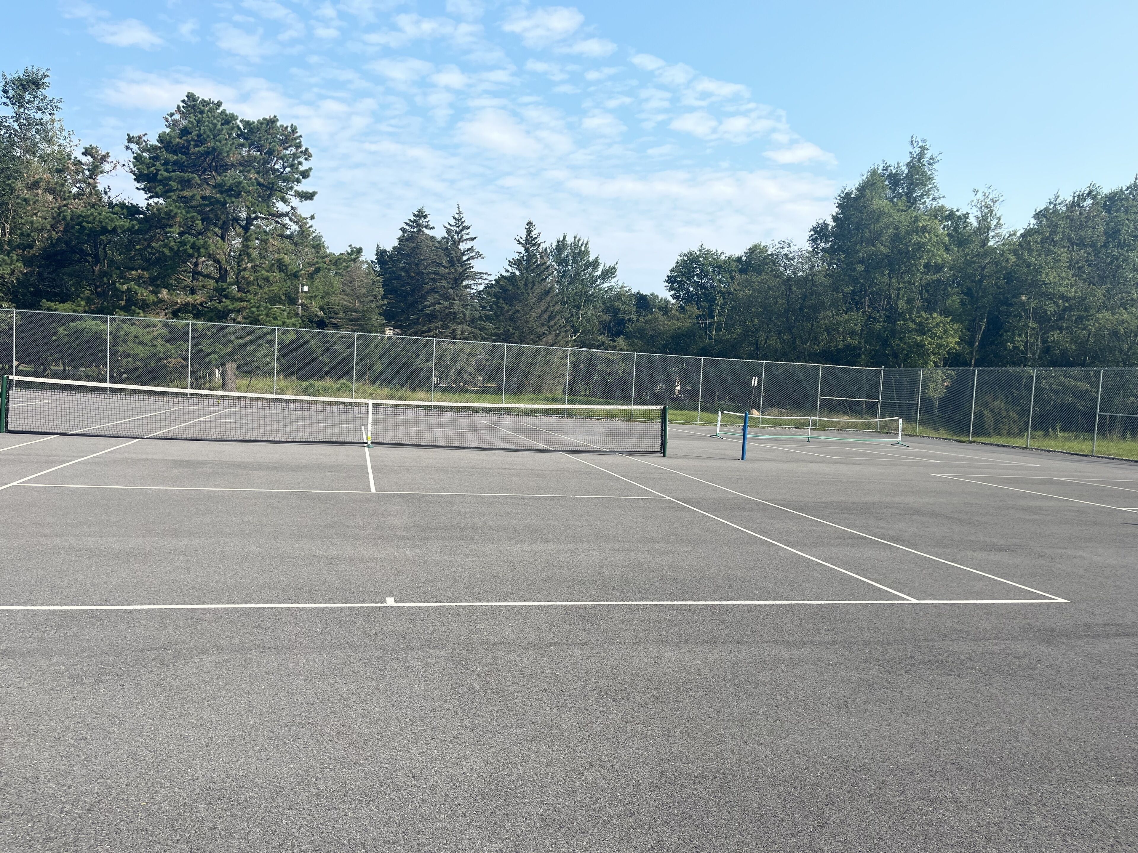 Cancha de tenis al aire libre con red, rodeada por una cerca y árboles.
