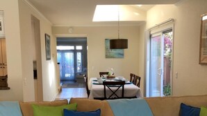 A living room with a beige sofa, green and blue cushions, a dining area with a table and chairs, and a view of the outdoors through a glass door. - "Welcome to Your Ultimate Huntington Beach Get-a-way! 3-Blocks to the Beach!  (Huntington Beach)