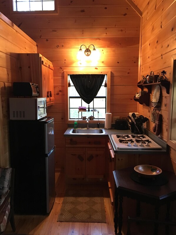 Eine kleine Küche mit Holzwänden, einem Kühlschrank, einer Mikrowelle, einem Spülbecken und einem Herd.